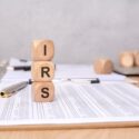 Wooden cubes with IRS abbreviation on a financial spreadsheet, pen and business background on a desk.